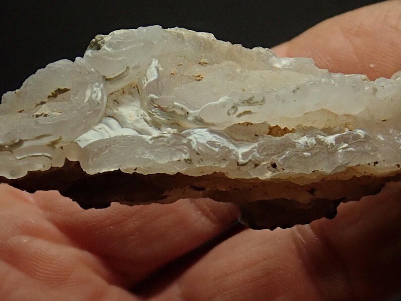 May include: A close-up of a layered stone, displaying a mix of white, beige, and light brown colours. The stone's surface has a wavy, textured appearance, with visible crystalline structures. The overall aesthetic suggests a natural, geological specimen.
