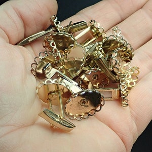 May include: A pile of gold-toned metal cuff links with a decorative, scalloped edge. The cuff links are in a hand.