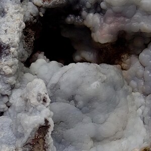 May include: Close-up of a blue and white agate geode with a cave-like opening. The geode has a rough, textured surface and is filled with small, white crystals.