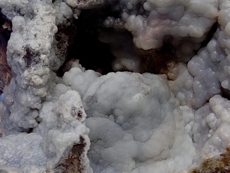May include: Close-up of a blue and white agate geode with a cave-like opening. The geode has a rough, textured surface and is filled with small, white crystals.