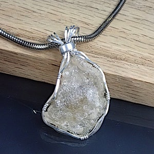 May include: A silver wire wrapped pendant featuring a clear, white, and gray, irregularly shaped stone. The pendant is attached to a silver chain.