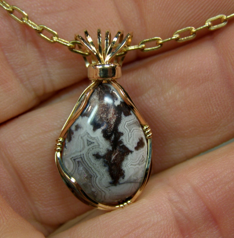 May include: A gold chain necklace with a pendant featuring a brown and white agate stone wrapped in gold wire.
