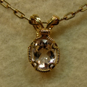 May include: A gold wire wrapped pendant featuring a clear oval gemstone. The pendant is attached to a gold chain.