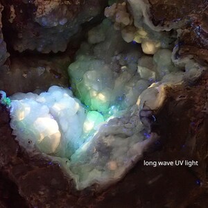 May include: A close-up of a geode with a white and green interior. The geode is illuminated with long wave UV light, causing the interior to glow a bright blue and green.