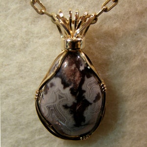 May include: A gold chain necklace with a pendant featuring a teardrop-shaped stone with brown and white swirling patterns, set in a gold wire frame.