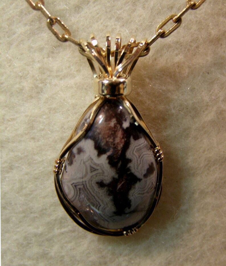 May include: A gold chain necklace with a pendant featuring a teardrop-shaped stone with brown and white swirling patterns, set in a gold wire frame.