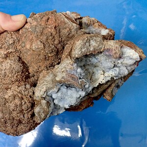 May include: A large, irregularly shaped rock with a rough, brown exterior. The rock has a cavity filled with white and blue crystals.