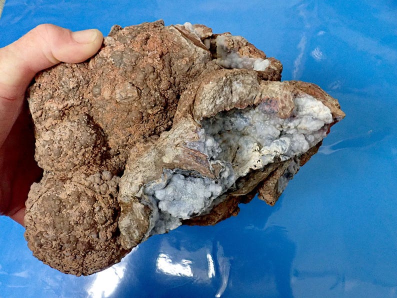 May include: A large, irregularly shaped rock with a rough, brown exterior. The rock has a cavity filled with white and blue crystals.