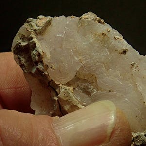 May include: A close-up of a mineral specimen showing a translucent, layered, white crystalline structure. The mineral has a rough, textured surface with beige and tan areas. The specimen is held in a hand.