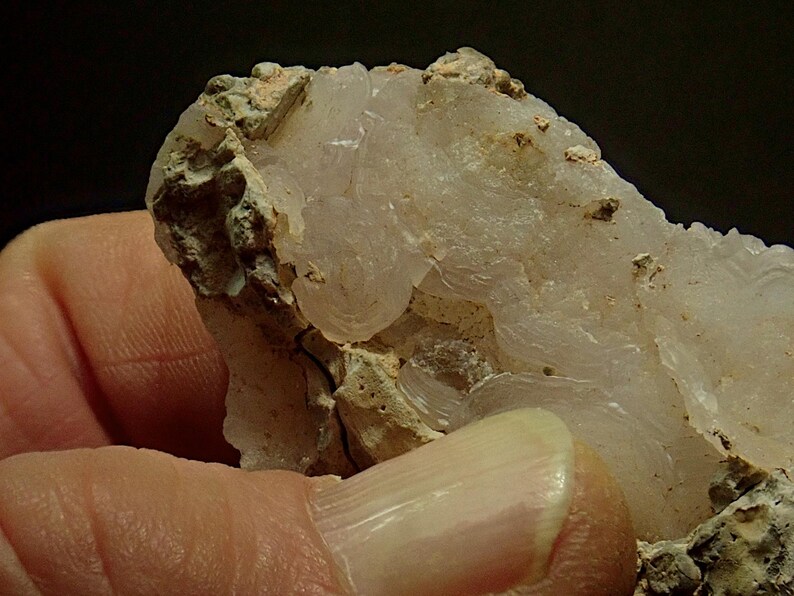 May include: A close-up of a mineral specimen showing a translucent, layered, white crystalline structure. The mineral has a rough, textured surface with beige and tan areas. The specimen is held in a hand.