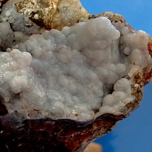 May include: A close-up of a geode with a light purple and white crystal formation. The geode is partially broken open, revealing the crystals inside. The geode is surrounded by a brown, rocky exterior.