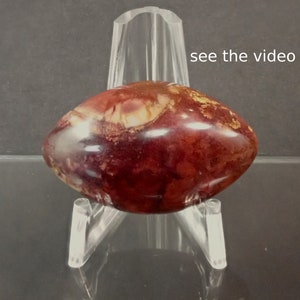 May include: A red, white, and gold agate stone with a swirling pattern. The stone is on a clear acrylic stand. See the video.
