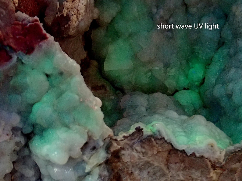 May include: A close-up of a green and white mineral specimen under short wave UV light. The mineral glows a bright green under the light.