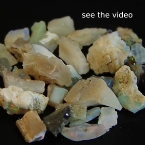 May include: A collection of rough opal stones in various shades of white, brown, and green. The stones are on a black surface. see the video