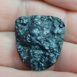 May include: A dark gray, irregularly shaped rock with a rough, textured surface. The rock has a metallic sheen and appears to be a meteorite.