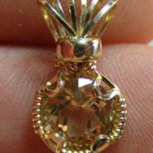 May include: A gold pendant featuring a faceted, light brown gemstone set in a delicate gold frame. The pendant has a unique, crown-like bail.