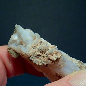 May include: Close-up of a mineral specimen, showing a light blue and white crystalline structure with a rough, textured surface. The mineral has a beige, earthy matrix with small, rounded formations.
