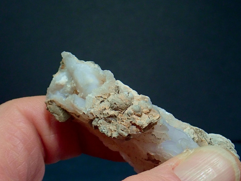 May include: Close-up of a mineral specimen, showing a light blue and white crystalline structure with a rough, textured surface. The mineral has a beige, earthy matrix with small, rounded formations.