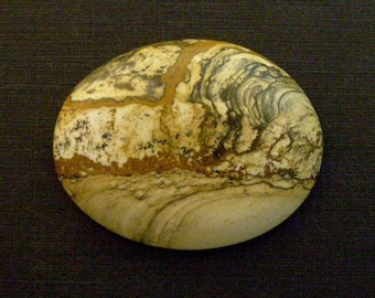 May include: A smooth, oval-shaped stone with a swirling pattern of brown, white, and gray. The stone has a natural, polished finish.