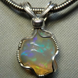 May include: A silver wire wrapped pendant featuring a white opal with iridescent blue and green flashes. The pendant is attached to a silver chain.