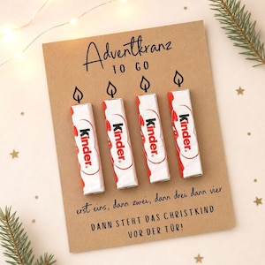 Pode incluir: Um cartão retangular castanho com o texto Adventkranz TO GO e quatro barras de chocolate Kinder fixadas verticalmente. Cada barra tem um desenho a traço preto de uma chama de vela por cima. O texto diz erst eins, dann zwei, dann drei dann vier DANN STEHT DAS CHRISTKIND VOR DER TÜR!