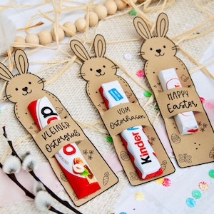 Könnte beinhalten: Oster-Geschenkanhänger in Hasenform, die Kinder-Schokoriegel halten. Die Anhänger aus braunem Karton tragen die Aufschriften "Kleiner Ostergruß", "Vom Osterhasen" und "Happy Easter". Verziert mit Eiern und Schmetterlingen.