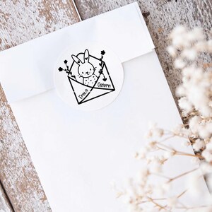May include: A white envelope with a black and white illustration of a bunny rabbit inside. The envelope has the text "Frohe Ostern" written on it.
