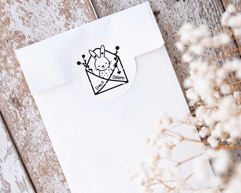 May include: A white envelope with a black and white illustration of a bunny rabbit inside. The envelope has the text "Frohe Ostern" written on it.