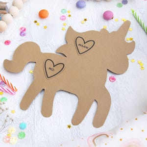 May include: A brown cardboard unicorn cutout with two heart-shaped stickers. The stickers say "WANN" and "WO:". The unicorn is surrounded by confetti and candles.