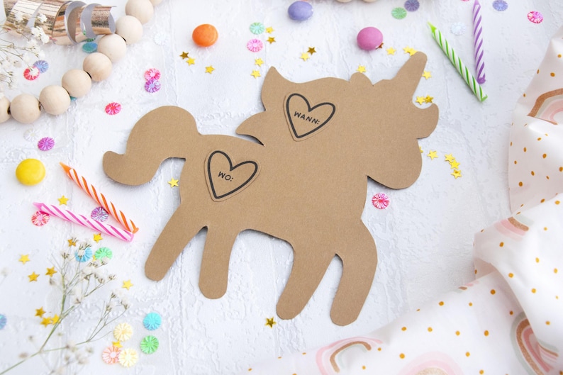 May include: A brown cardboard unicorn cutout with two heart-shaped stickers. The stickers say "WANN" and "WO:". The unicorn is surrounded by confetti and candles.