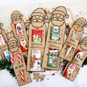 Könnte beinhalten: Eine Sammlung weihnachtlicher Geschenkanhänger in Form von Weihnachtsmännern, die jeweils eine kleine Leckerei wie Süßigkeiten oder Schokolade enthalten. Die Anhänger tragen deutsche Sätze wie "Liebe Grüße vom Nikolaus" und "Frohe Weihnachten".