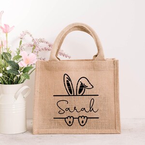 K&ouml;nnte beinhalten: Eine braune Jute-Tragetasche mit schwarzen Hasenohren und dem Namen "Sarah" auf der Vorderseite. Die Tasche hat zwei Henkel und ist perfekt f&uuml;r den Transport kleiner Gegenst&auml;nde.