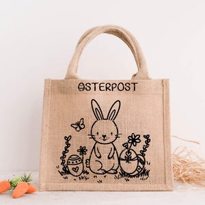 May include: A brown burlap tote bag with black handles and a black bunny rabbit design. The bag has the text "OSTERPOST" printed on the front.
