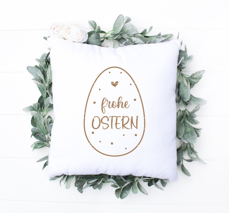 K&ouml;nnte beinhalten: Ein wei&szlig;es Kissen mit einem braunen Osterei-Design und dem Text "frohe Ostern".