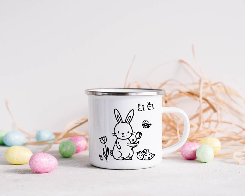 May include: White enamel mug featuring a black illustration of a rabbit holding a flower, with a butterfly and ladybug. The mug has a silver rim and a white handle. Colourful Easter eggs are scattered around the mug.