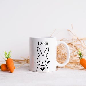 May include: White ceramic mug with a black outline of a bunny with a heart and the name Luisa printed on it.