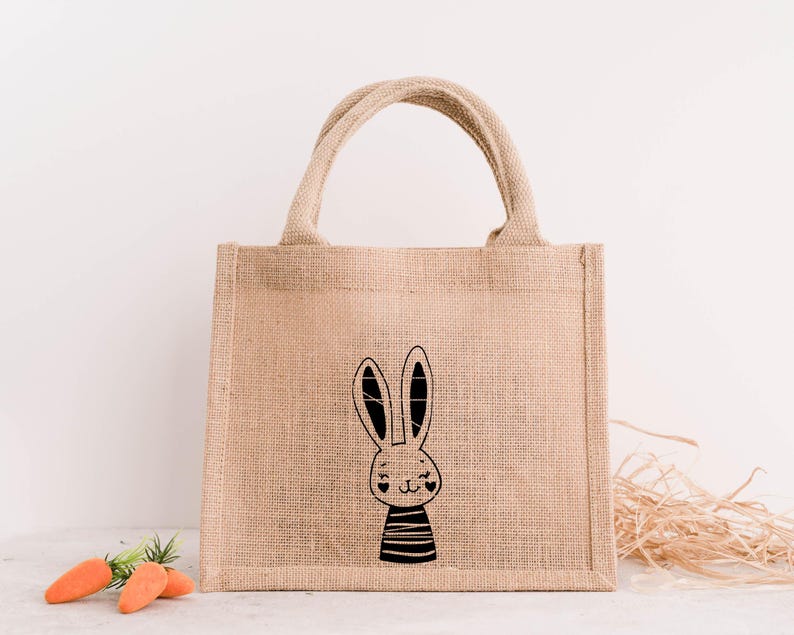 Op de afbeelding: Een beige jute draagtas met een zwart-witte konijnenillustratie. Het konijn draagt een gestreept shirt en heeft twee harten als ogen.