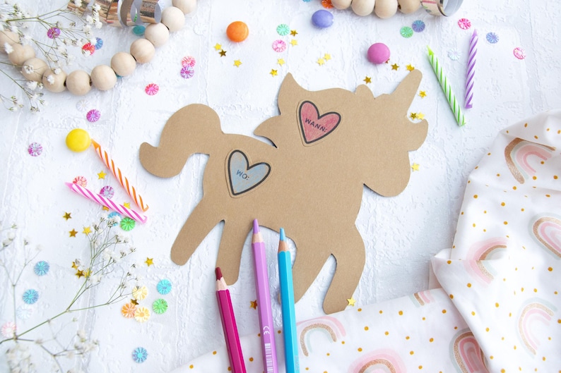 May include: A brown cardboard unicorn cutout with two heart-shaped stickers that say "Wanna" and "Pic." The unicorn is surrounded by colorful confetti, candles, and pencils.