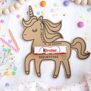 May include: A brown cardboard unicorn cutout with a Kinder chocolate bar inside. The unicorn has a black outline and the words "Einladung zu meinem Geburtstag" written on it. The unicorn is surrounded by colorful confetti and candles.