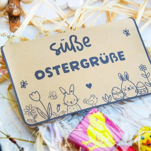 May include: A brown paper bag with a cute Easter greeting that says "S&uuml;&szlig;e Ostergr&uuml;&szlig;e" and features a bunny, flowers, and eggs. The bag is filled with chocolate Easter treats.