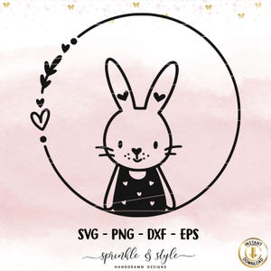 May include: Black and white line art illustration of a bunny wearing a dress with hearts. The bunny is inside a circle with a wreath of leaves and hearts around it.