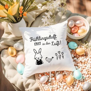 May include: White pillow with black text that reads "Fr&uuml;hlingsduft liegt in der Luft!" and a black and white illustration of a bunny, a bird, and flowers.
