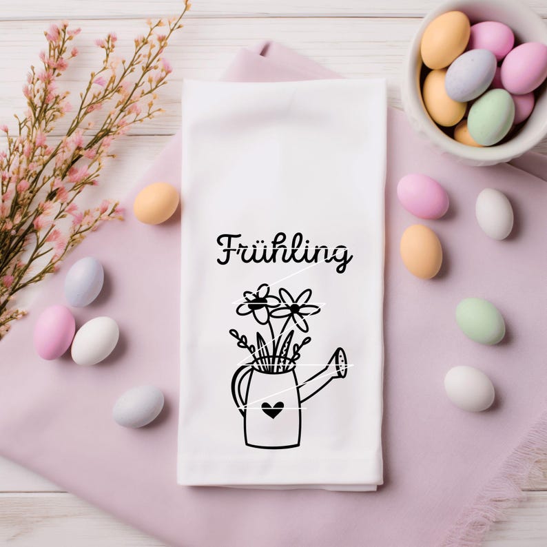 May include: White tea towel with a black and white illustration of a watering can filled with flowers. The text "Fr&uuml;hling" is printed above the illustration.