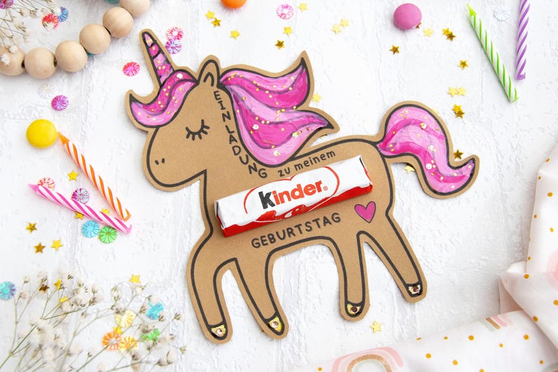 May include: A brown cardboard unicorn cutout with pink glitter mane and tail. The unicorn has a chocolate bar with the text "Kinder" on it, and the text "Einladung zu meinem Geburtstag" on the side.