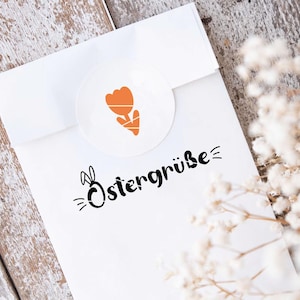 K&ouml;nnte beinhalten: Wei&szlig;er Umschlag mit einem schwarzen und orangefarbenen Ostergru&szlig;, der "Ostergr&uuml;&szlig;e" mit einem Hasen und einer Tulpe sagt.