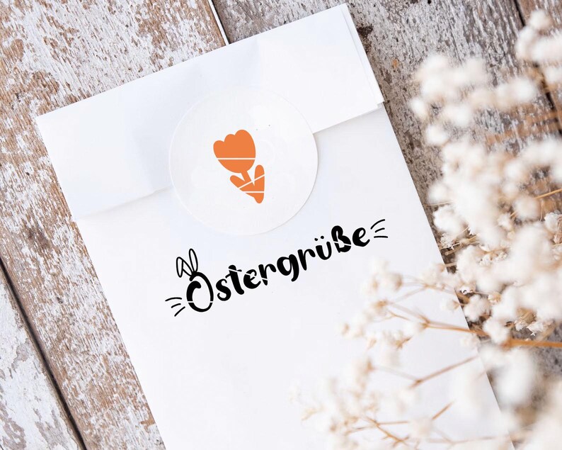 K&ouml;nnte beinhalten: Wei&szlig;er Umschlag mit einem schwarzen und orangefarbenen Ostergru&szlig;, der "Ostergr&uuml;&szlig;e" mit einem Hasen und einer Tulpe sagt.