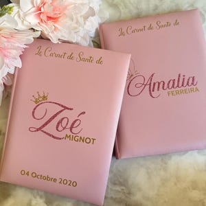 May include: Two pink health record books with gold lettering and glitter accents. One book is personalized with the name "Zo&eacute; MIGNOT" and the date "04 Octobre 2020". The other book is personalized with the name "Amalia FERREIRA".