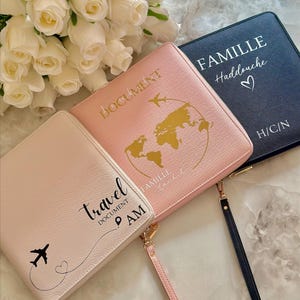May include: Three pink and white travel document holders with gold accents. The holders have different text on them, including "Travel Document", "Document", "Famille", and "Haddouche".