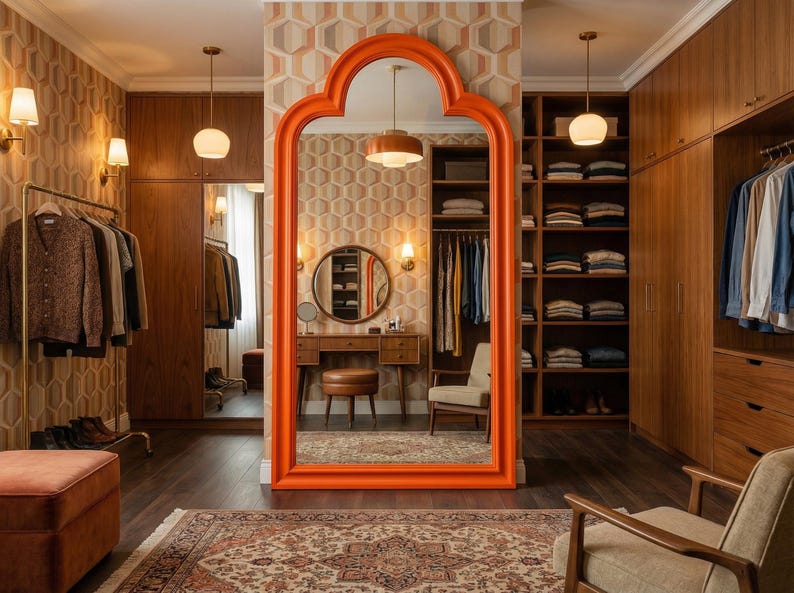May include: A stylish walk-in closet with a large orange framed mirror. The room features wooden cabinets, a clothing rack, and a patterned rug. The walls are decorated with a geometric wallpaper, and the room is illuminated by warm lighting.