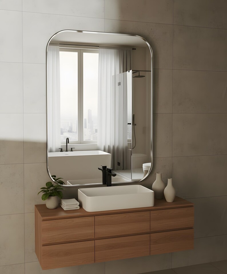 May include: A contemporary bathroom scene featuring a wooden vanity unit with a white rectangular sink and black tap. A large, rounded mirror reflects a window and shower. The vanity has six drawers. Two white vases and a plant are on the counter.